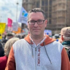 Man with glasses looking at the camera, wearing a zip-up hoodie.