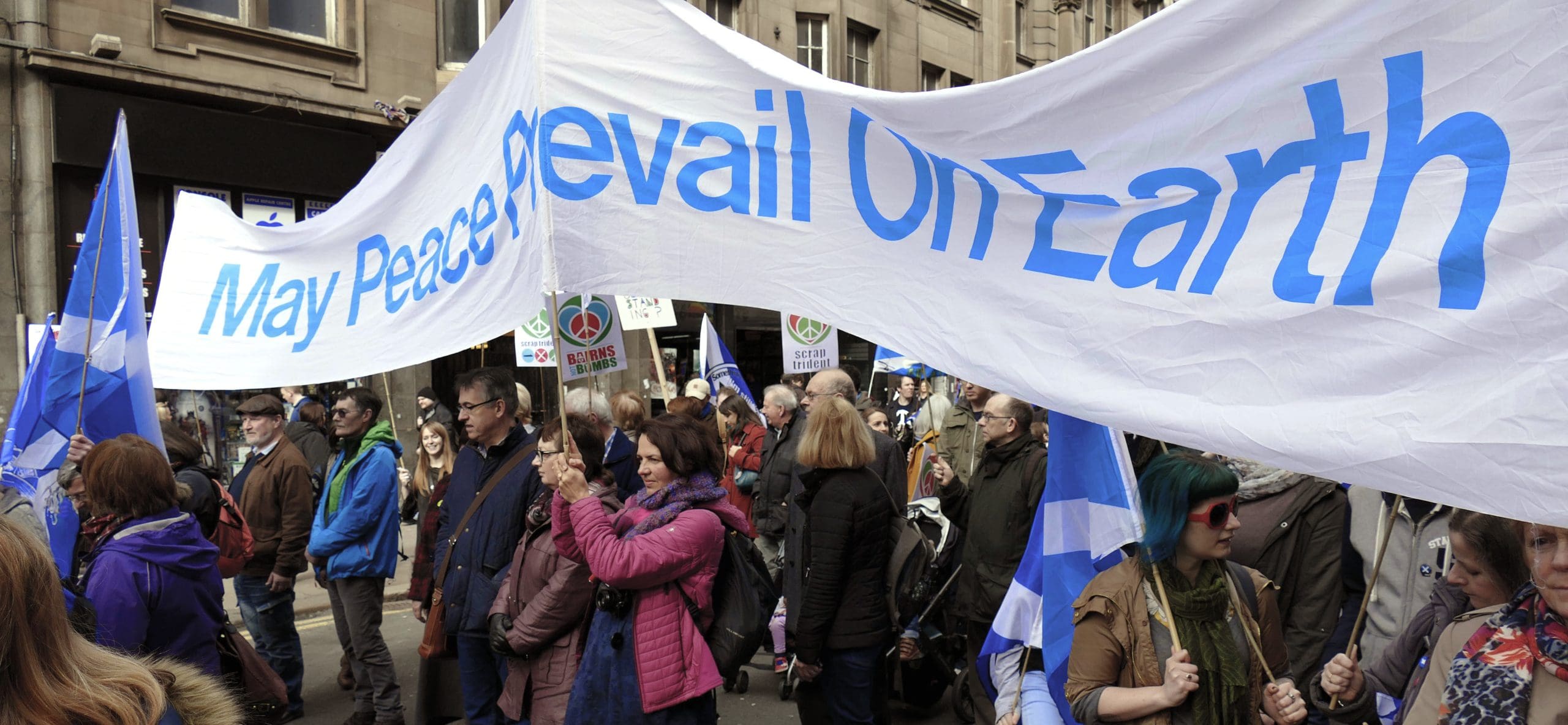 People walking with a May Peace Prevail on Earth banner