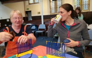 Two women drink tea and chat while weaving at ColumbaFest