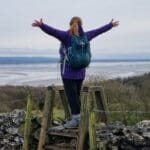 Woman standing on a stile climbing over a wall.