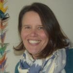 woman smiling at camera with a chain of peace cranes hanging beside her