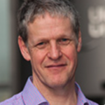 Man with greying hair and a lilac shirt