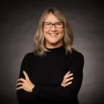 Woman wearing a black jumper with glasses and shoulder length hair.