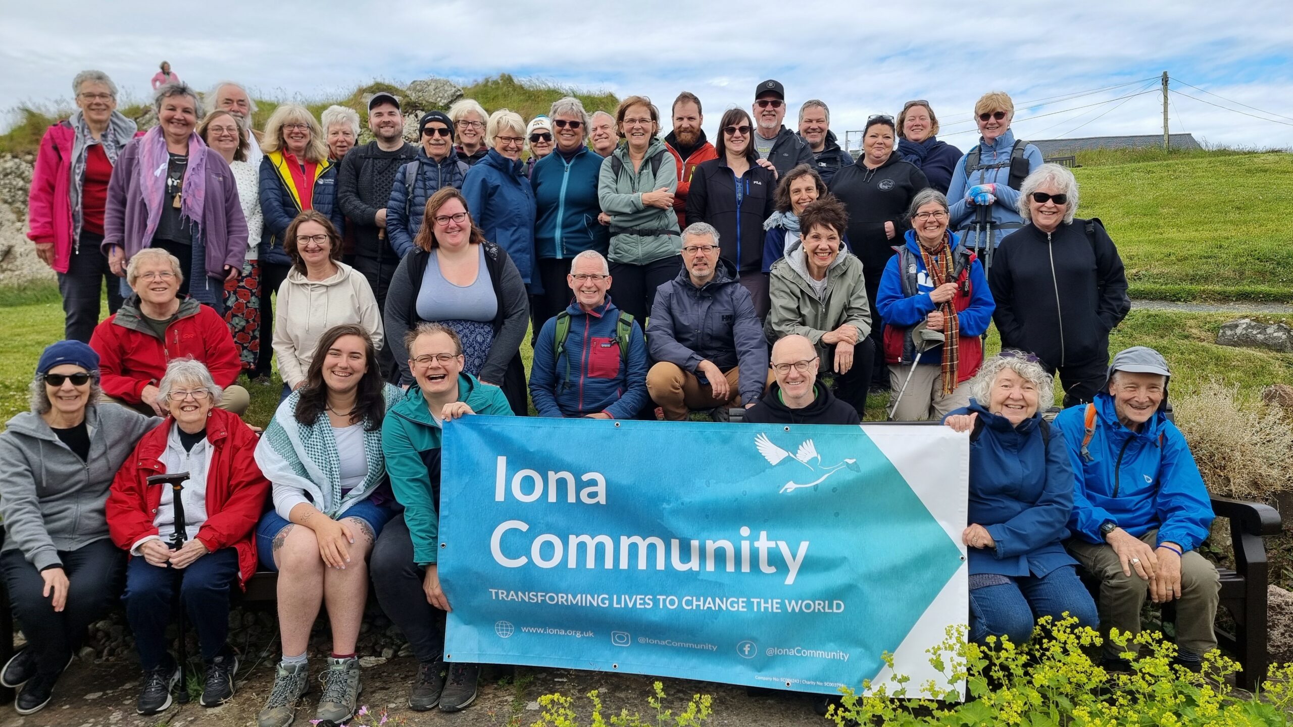 Group photo against a hill and sky. People hold a blue Iona Community banner.
