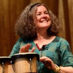 A woman in a green shirt playing bongo drums