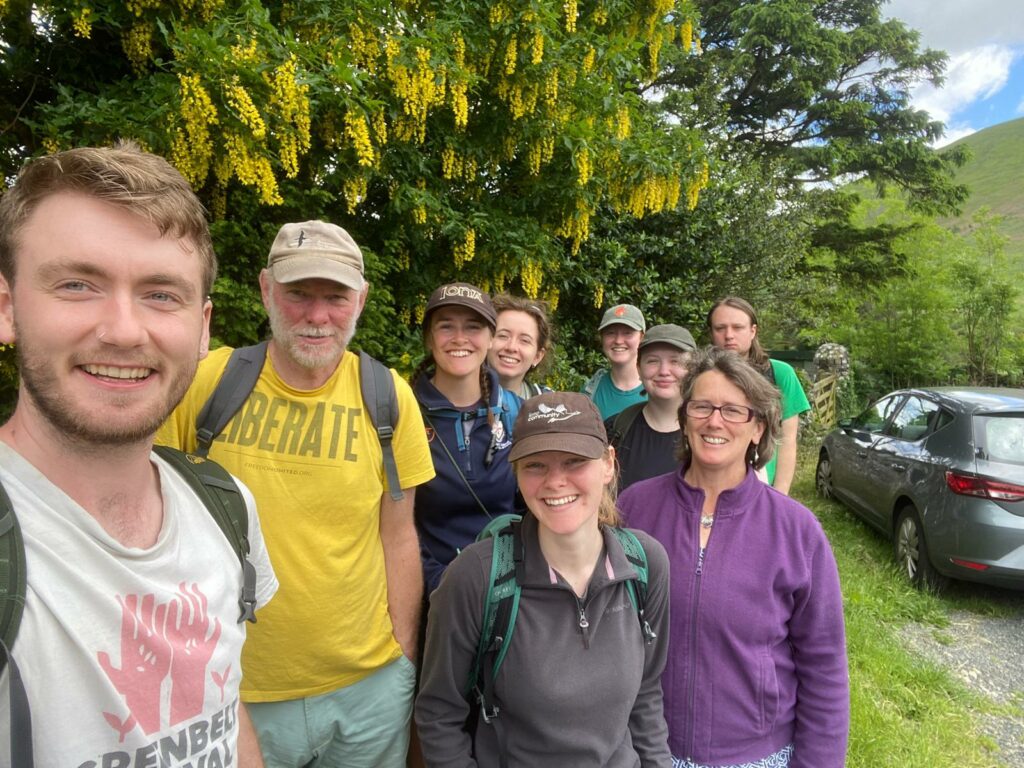 A selfie with nine people outside underneath a tree with yellow flowers smiling at camera