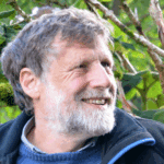 Man with brown hair and grey beard and a navy fleece looking to the right of camera and smiling. 