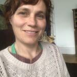 Woman with auburn hair and a cream jumper smiling at the camera.