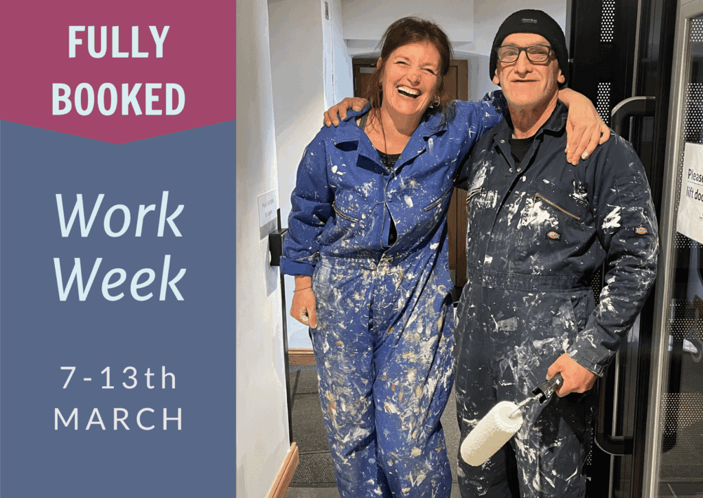 Two people in boilers suits covered in paint laughing at the camera.